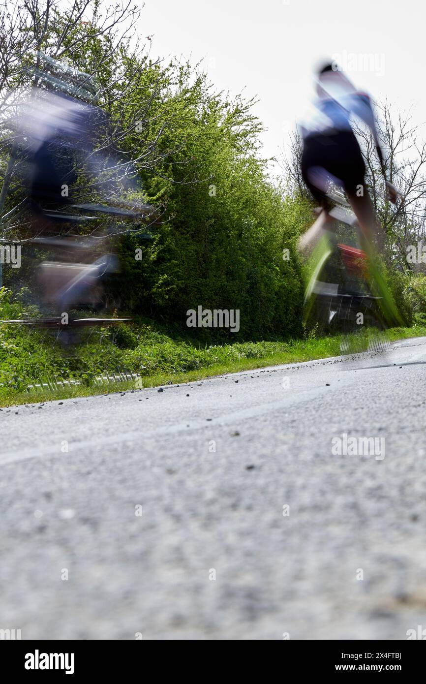 Zwei Menschen, die auf einer Landstraße auf Rennrädern fahren, in Bewegung und unfokussiert Stockfoto
