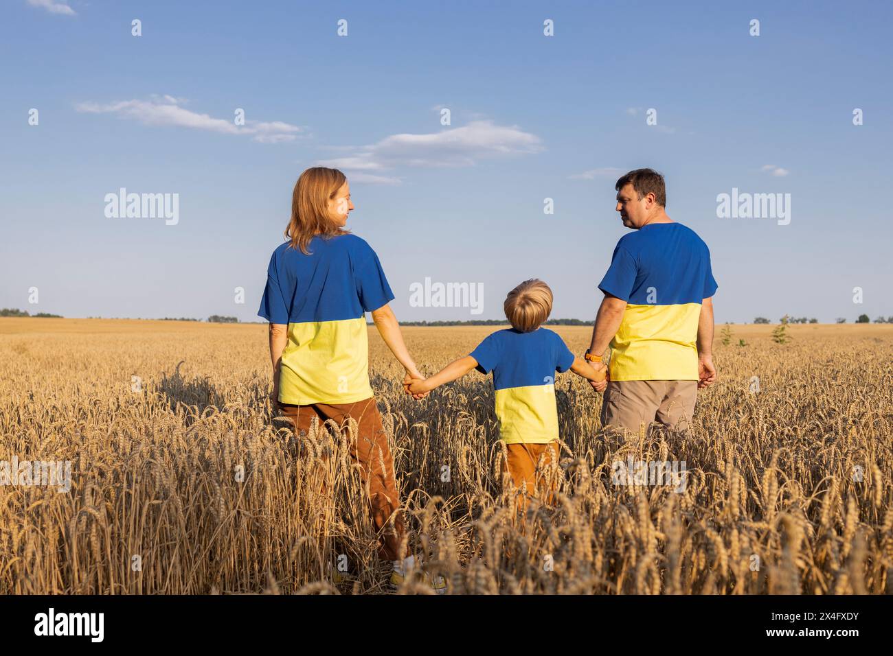 Ukrainische Familie in identischen gelben und blauen T-Shirts steht zwischen Weizenohren auf dem Feld. Stoppt den Krieg. Stolz auf deine Nation, Unterstützung, glaube an den Sieg Stockfoto