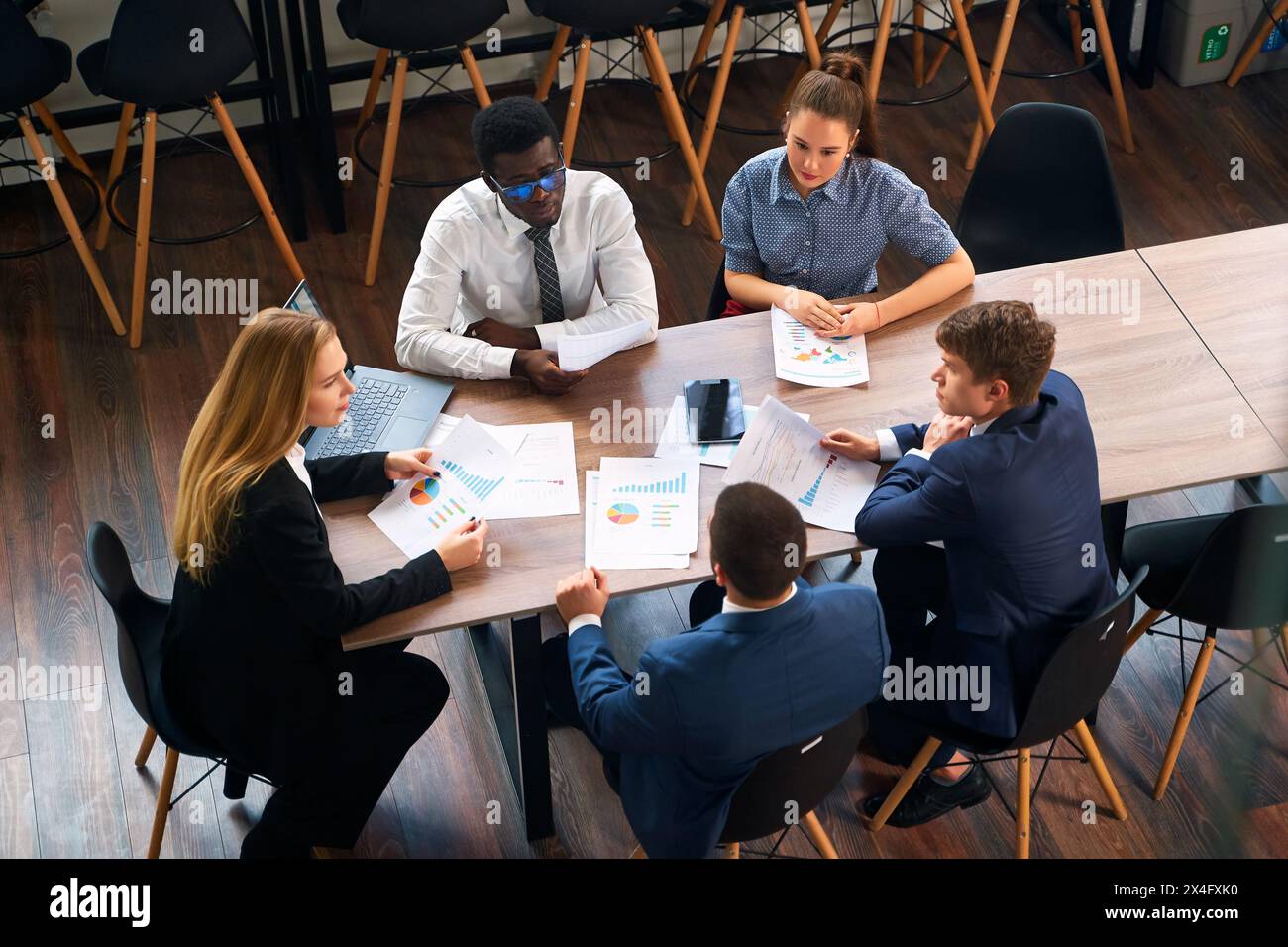 Weibliche CEO leitet in einer Strategiesitzung in modernen Büros verschiedene Teams, mit Diagrammen, Laptop für datengesteuerte Entscheidungen. Profis beteiligen sich an Stockfoto