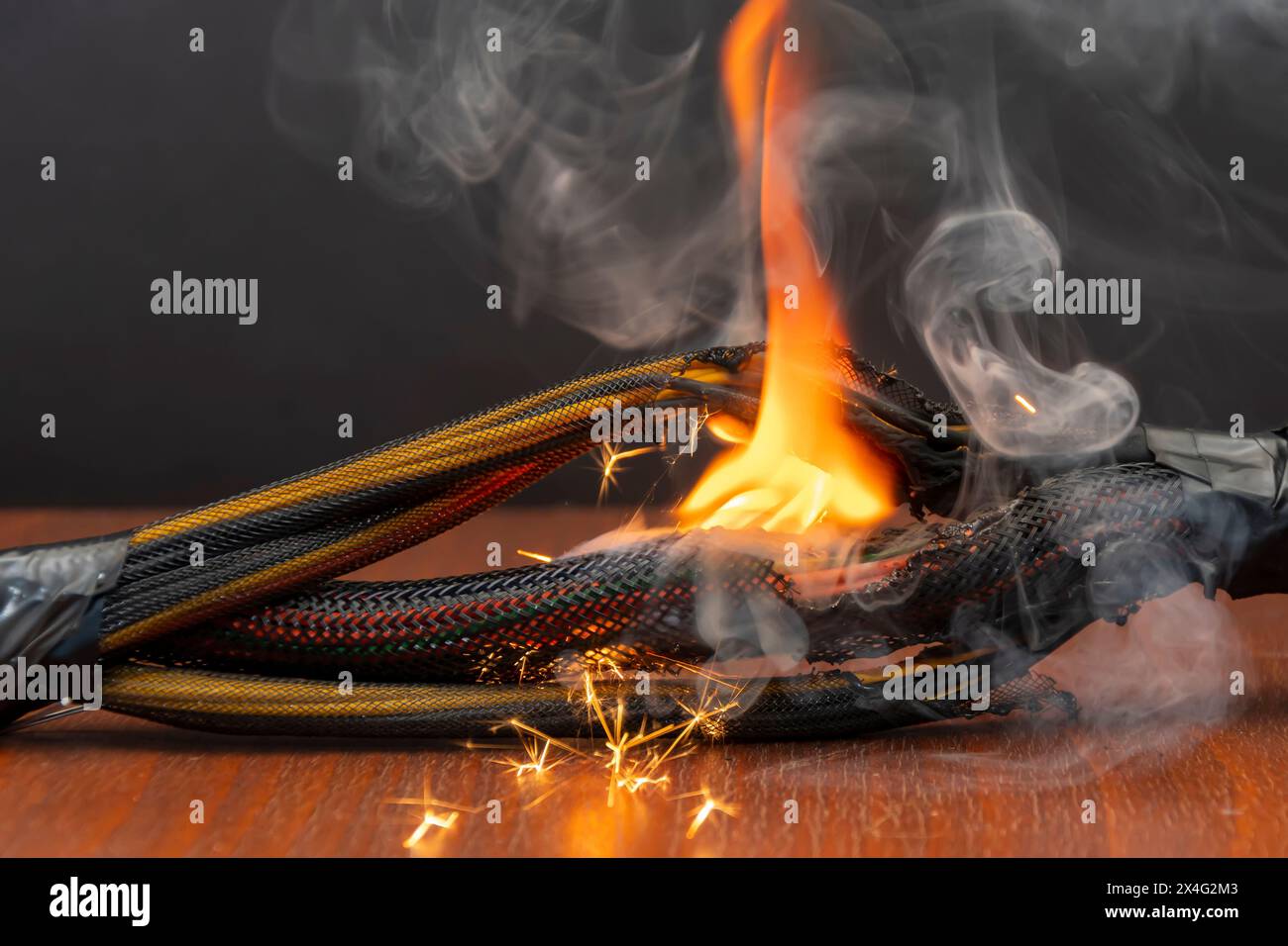 Elektrische Leitungen und Kabel sind auf einem dunklen Hintergrund beleuchtet. Ein Kurzschluss in den verdrillten Kabeln des Computers. Flammen, Funken und Rauch. Stockfoto