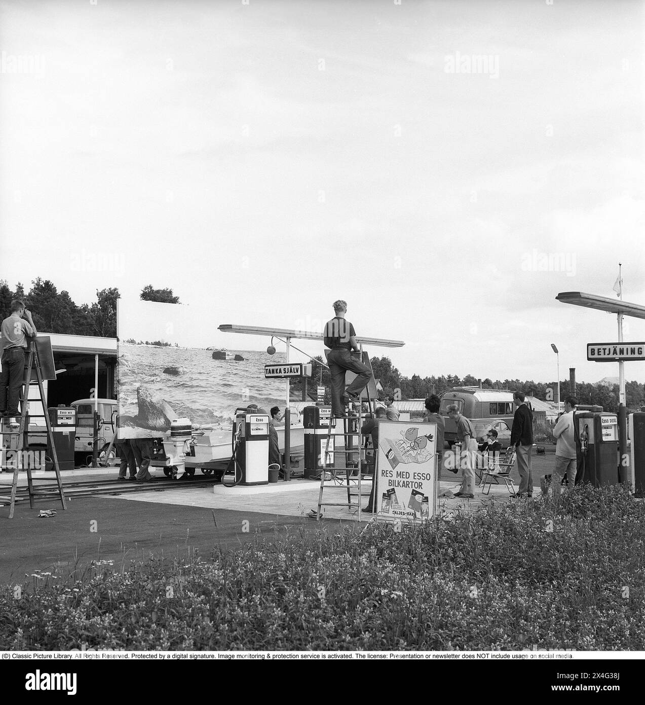 ESSO-Tankstelle im Jahr 1963. Die Firma Svenska Esso war eine Marke in Schweden zwischen 1939 und 1987, als die Bahnhöfe ihren Namen in den Namen des neuen Eigentümers Statoil änderten. An der Tankstelle wird ein Werbespot gefilmt, in dem ein Motorboot neben den Gaspumpen steht. Ein Hintergrund, der ein Meer darstellt, wird als Hintergrund verwendet. Kristoffersson Ref. DC135-9 Stockfoto