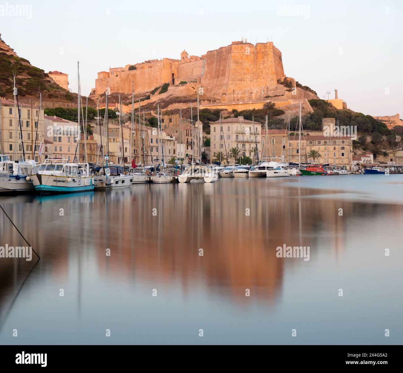 Bonifacio, Corse-du-Sud, Korsika, Frankreich. Blick über den Hafen auf die Zitadelle, die Morgendämmerung, die Bastion de l'Etendard spiegelt sich im ruhigen Wasser. Stockfoto