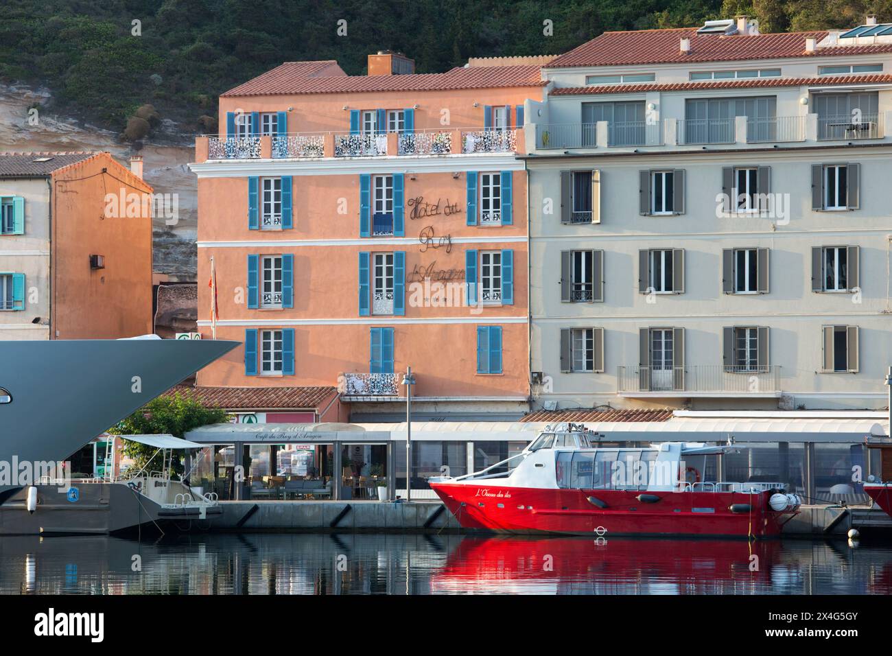 Bonifacio, Corse-du-Sud, Korsika, Frankreich. Blick vom Kai über den Hafen auf die pastellrosa Fassade des Hôtel du Roy d'Aragon, Sonnenaufgang. Stockfoto