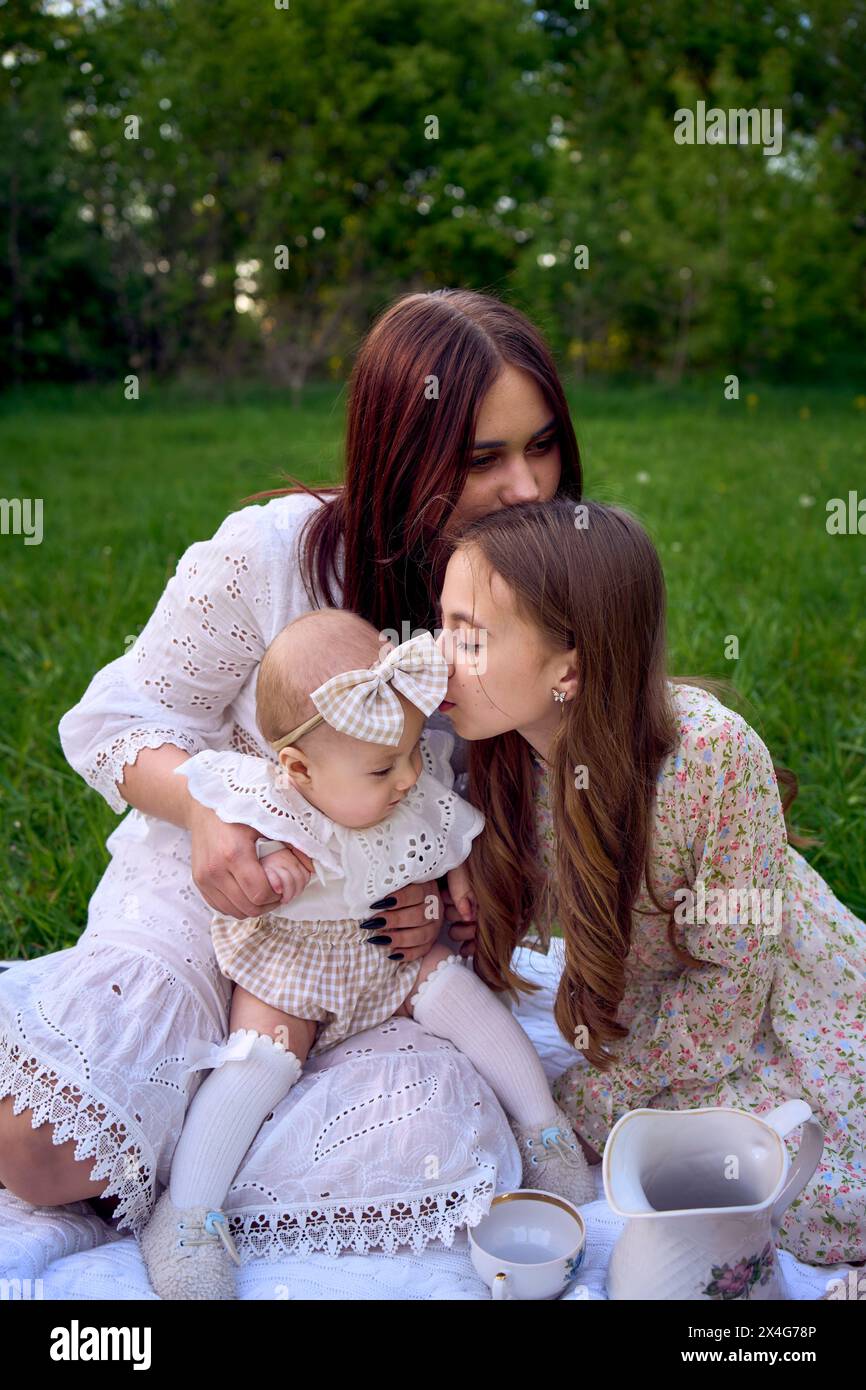Die Schwestern unterschiedlichen Alters umarmen sich zärtlich bei einem Picknick im Garten Stockfoto