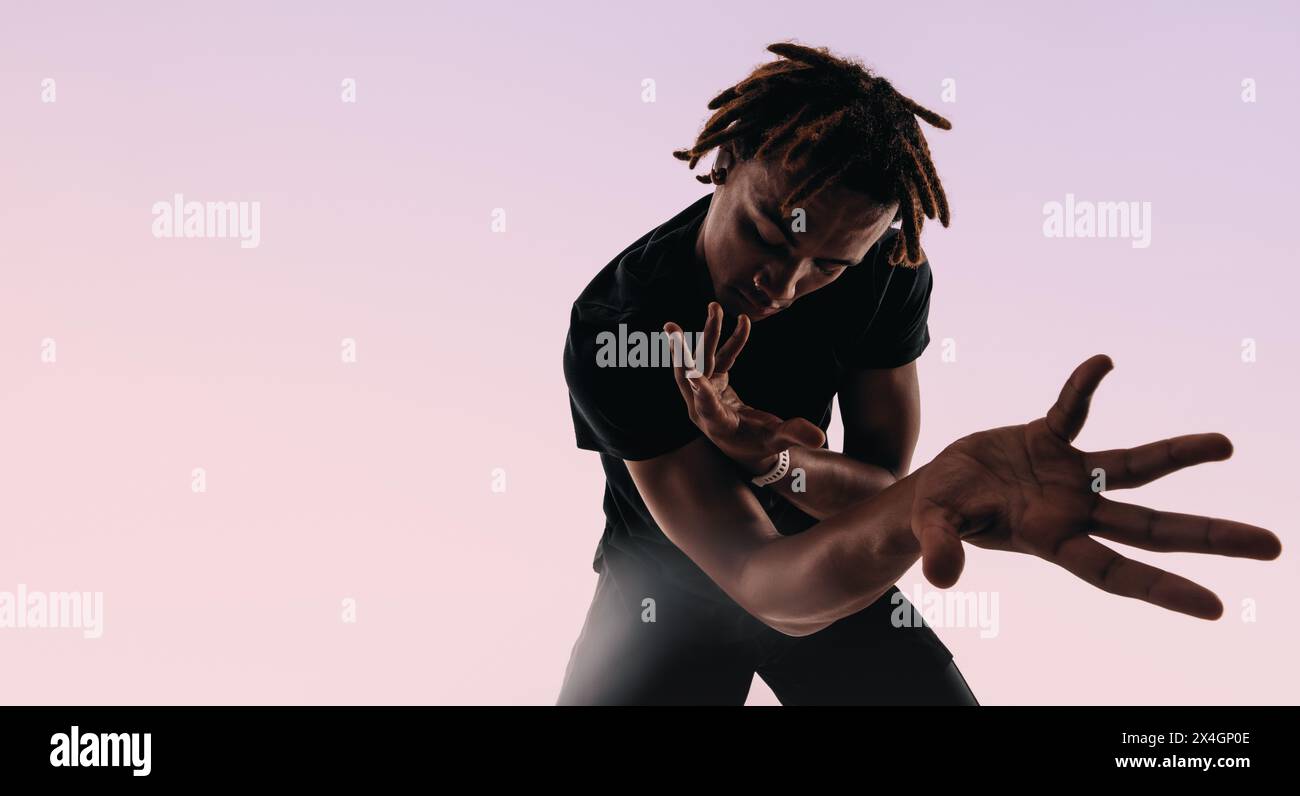 Der rhythmische Gen Z Männchen tanzt energetisch in einem Studio, seine expressiven Bewegungen erzeugen eine künstlerische Silhouette vor rosa Hintergrund. Stockfoto