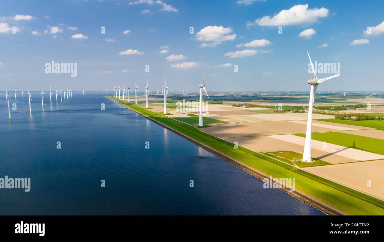 Ein ruhiger, großer Wasserkörper, umgeben von Windmühlen, die aktiv Strom mit der Kraft des Windes erzeugen. Stockfoto