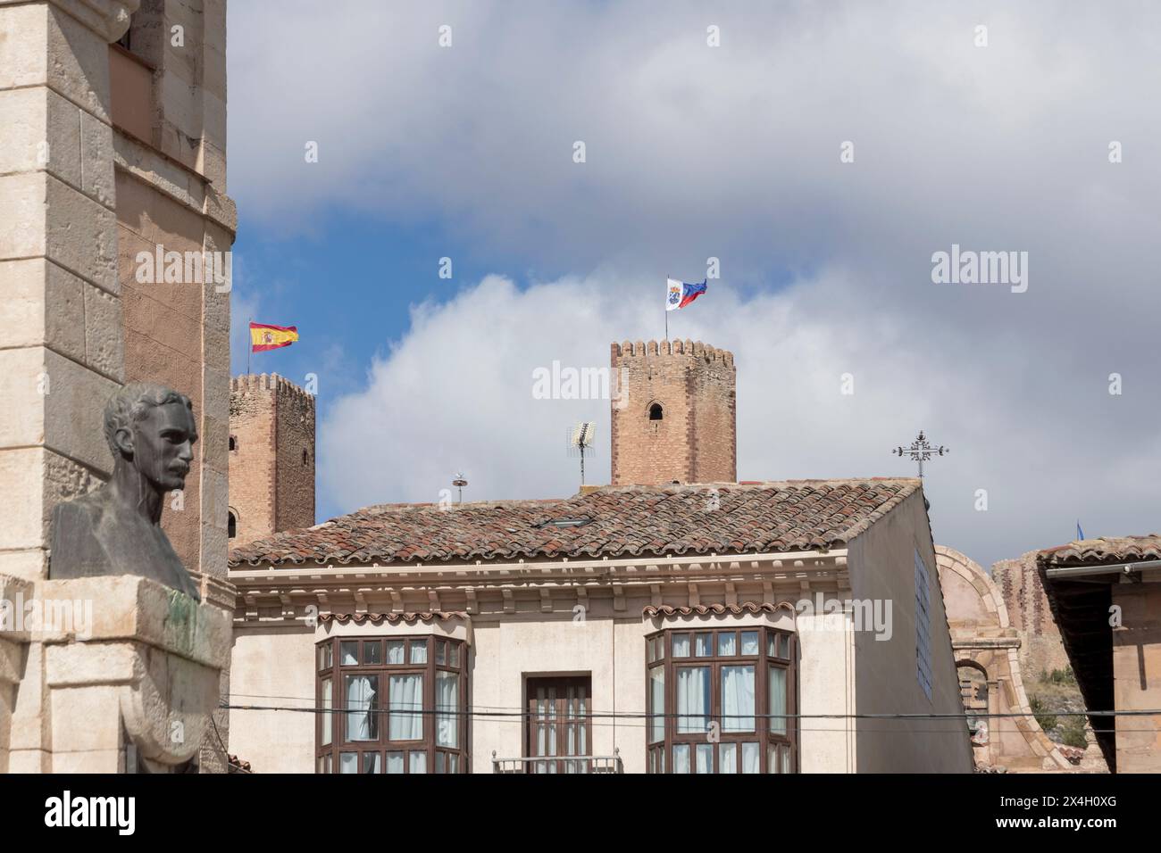 Eine ruhige, historische Szene in Spanien mit einer Steinbüste, Gebäuden und spanischen Flaggen unter einem bewölkten Himmel Stockfoto