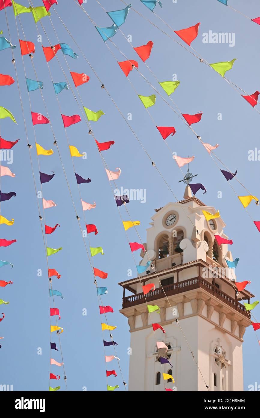 Majestätischer Uhrenturm mit bunten Fahnen, die im Wind winken, verleiht dem historischen Gebäude vor dem klaren blauen Himmel eine festliche Note Stockfoto