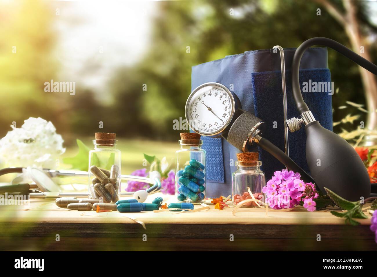 Konzept pflanzlicher Naturheilmittel zur Behandlung von Blutdruckproblemen mit Glasflaschen, Blutdruckmessgerät und Holzblüten Stockfoto