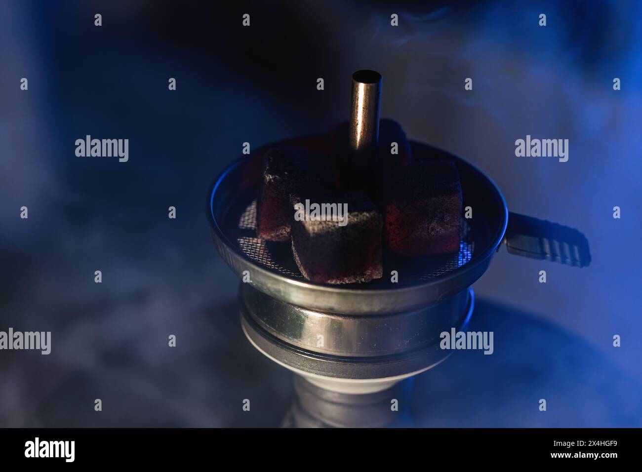 Nahaufnahme glühender Kohlen auf aromatischem Tabak in einer Shisha-Schüssel, die Rauch in einer dunklen, stimmungsvollen Umgebung in einer traditionellen Shisha Lounge im Nahen Osten ausstrahlt. Stockfoto