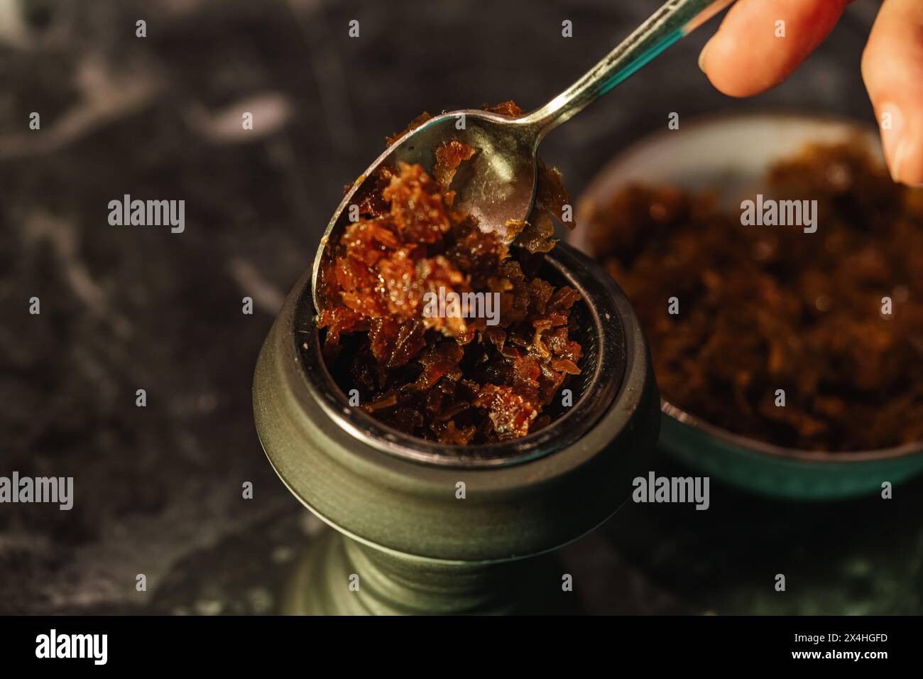 In einer Shisha-Bar auf einem Marmortisch in einer Shisha-Bar wird aromatisierter Tabak in eine Shisha-Schüssel geschüttet, wodurch Textur und Details betont werden Stockfoto