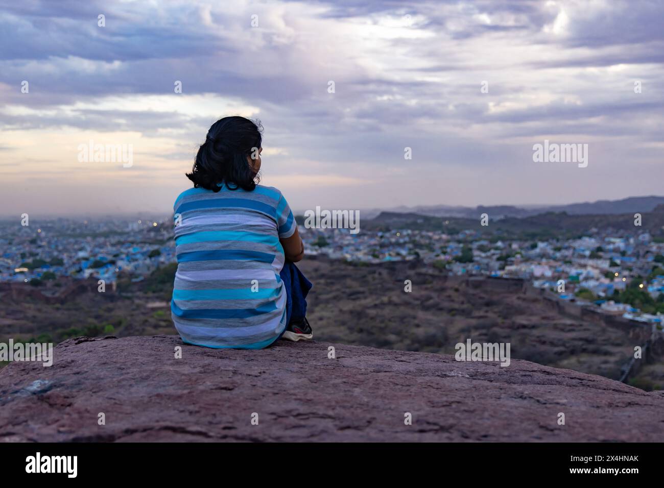 Isolieren Sie Mädchen, die die Stadtlandschaft auf dem Gipfel des Berges mit dramatischem Himmel in der Abenddämmerung beobachten, das Bild wird im mehrangarh jodhpur rajasthan india aufgenommen. Stockfoto