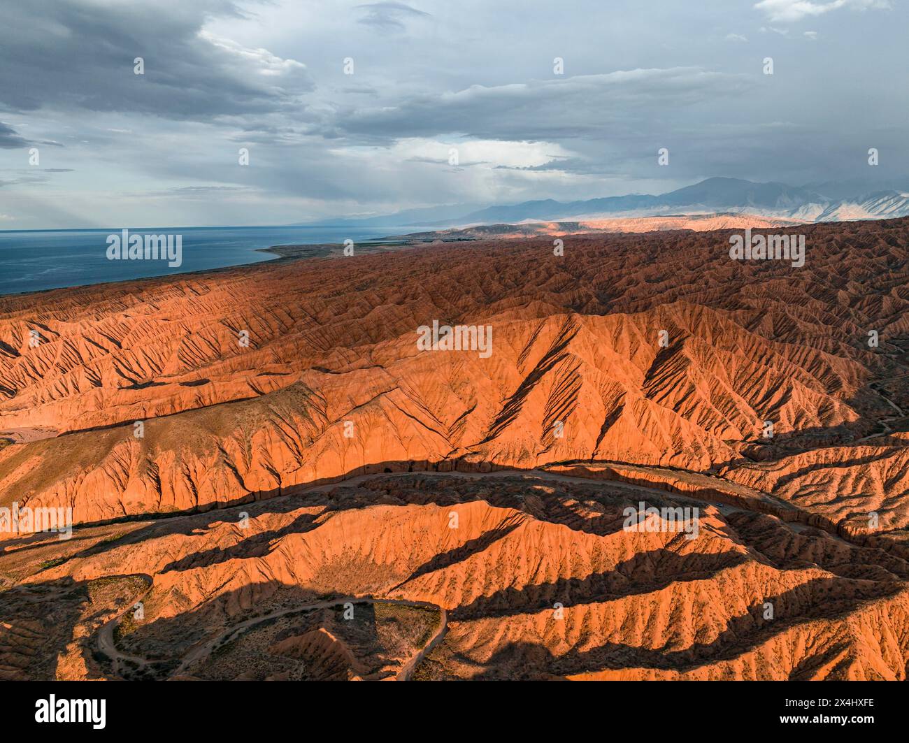 Der Canyon verläuft durch die Landschaft, der Issyk Kul Lake, hinter weißen Gipfeln der Tien Shan Mountains, dramatische karge Landschaft mit erodierten Hügeln, Badlands Stockfoto