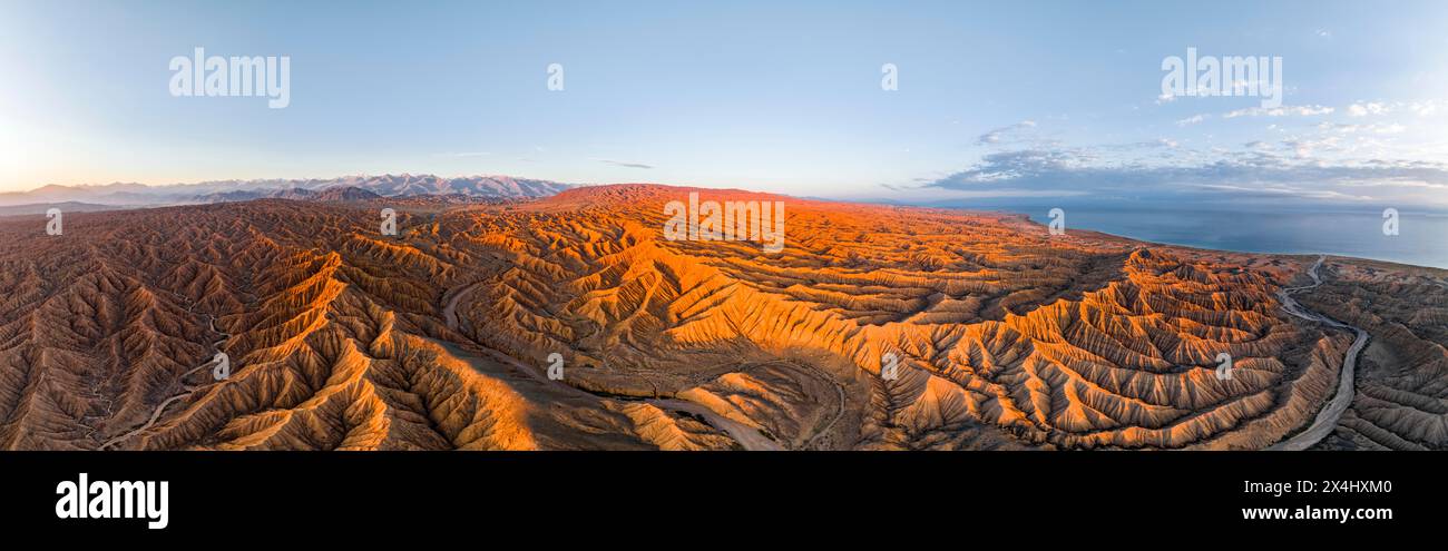 Der Canyon verläuft durch die Landschaft, der Issyk Kul Lake, hinter weißen Gipfeln der Tien Shan Mountains, dramatische karge Landschaft mit erodierten Hügeln, Badlands Stockfoto