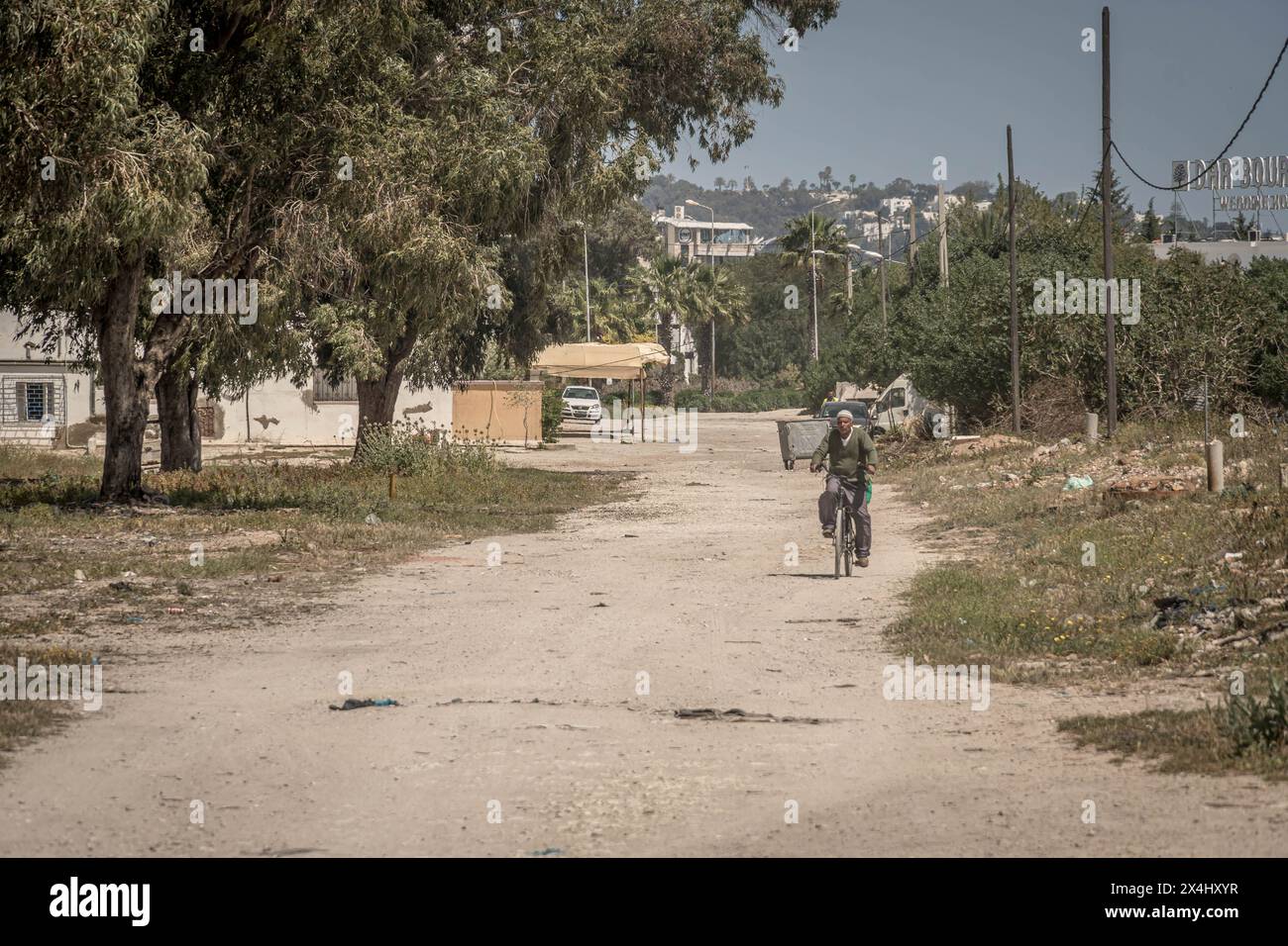 Die arme Nachbarschaft in Tunis, ein Mann auf dem Fahrrad, die staubige Straße an einem heißen Sommertag in Tunesien. Stockfoto