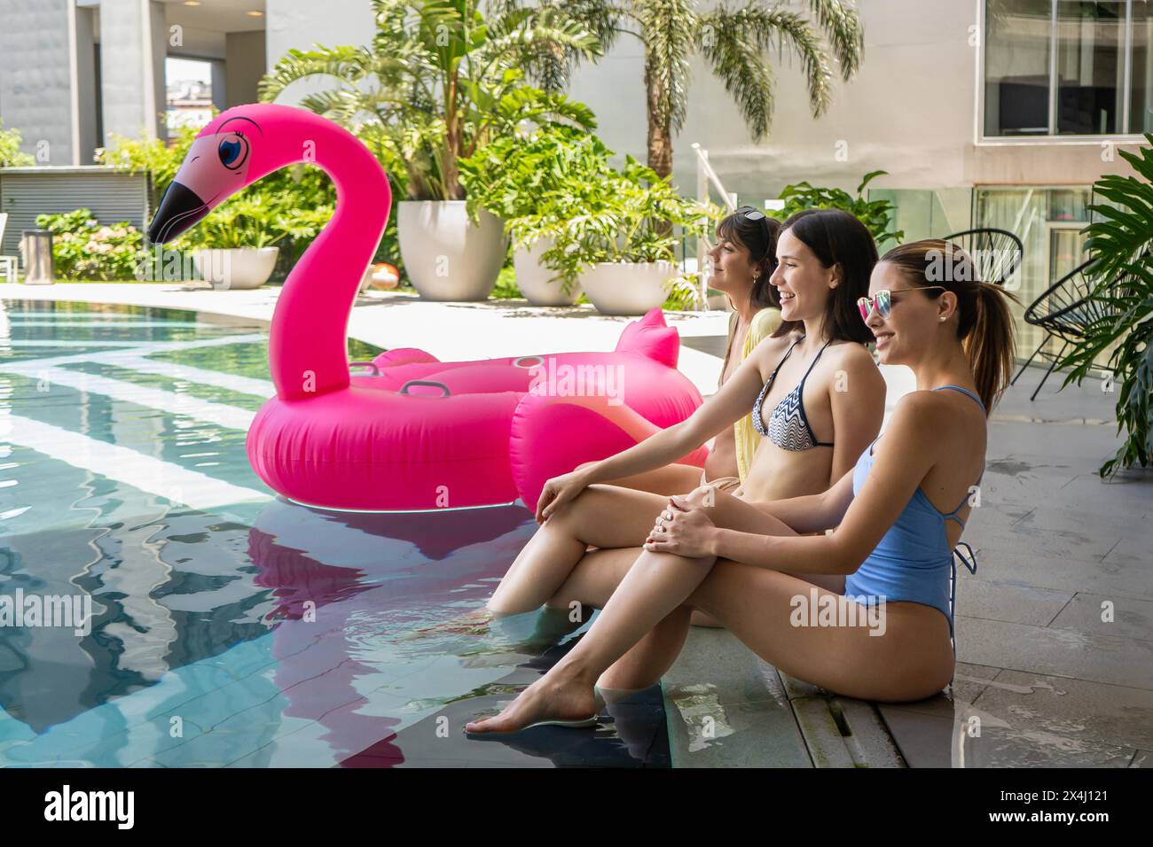 Drei Frauen sitzen in einem Pool mit einem rosafarbenen Flamingowagen. Sie lächeln und genießen ihre Zeit Stockfoto