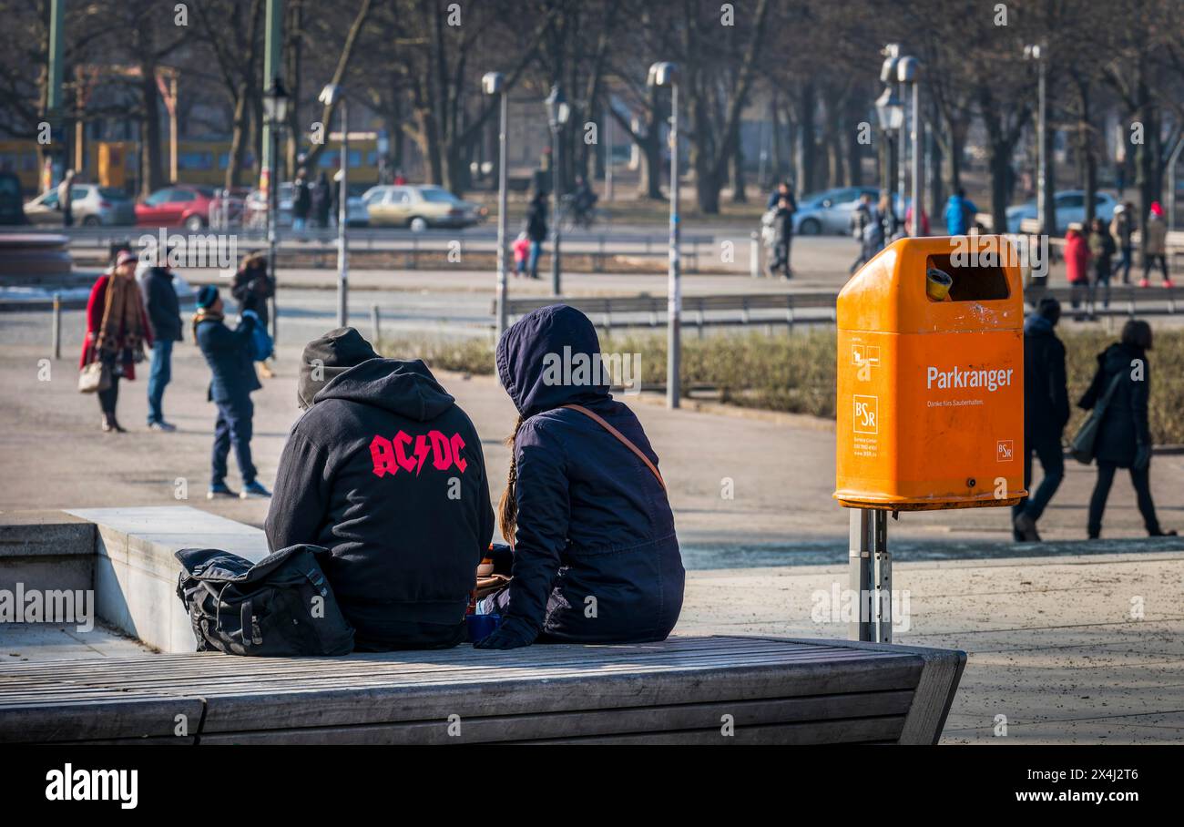 Junge Menschen, die neben einem orangefarbenen Abfalleimer der Berliner Stadtreinigung sitzen Stockfoto