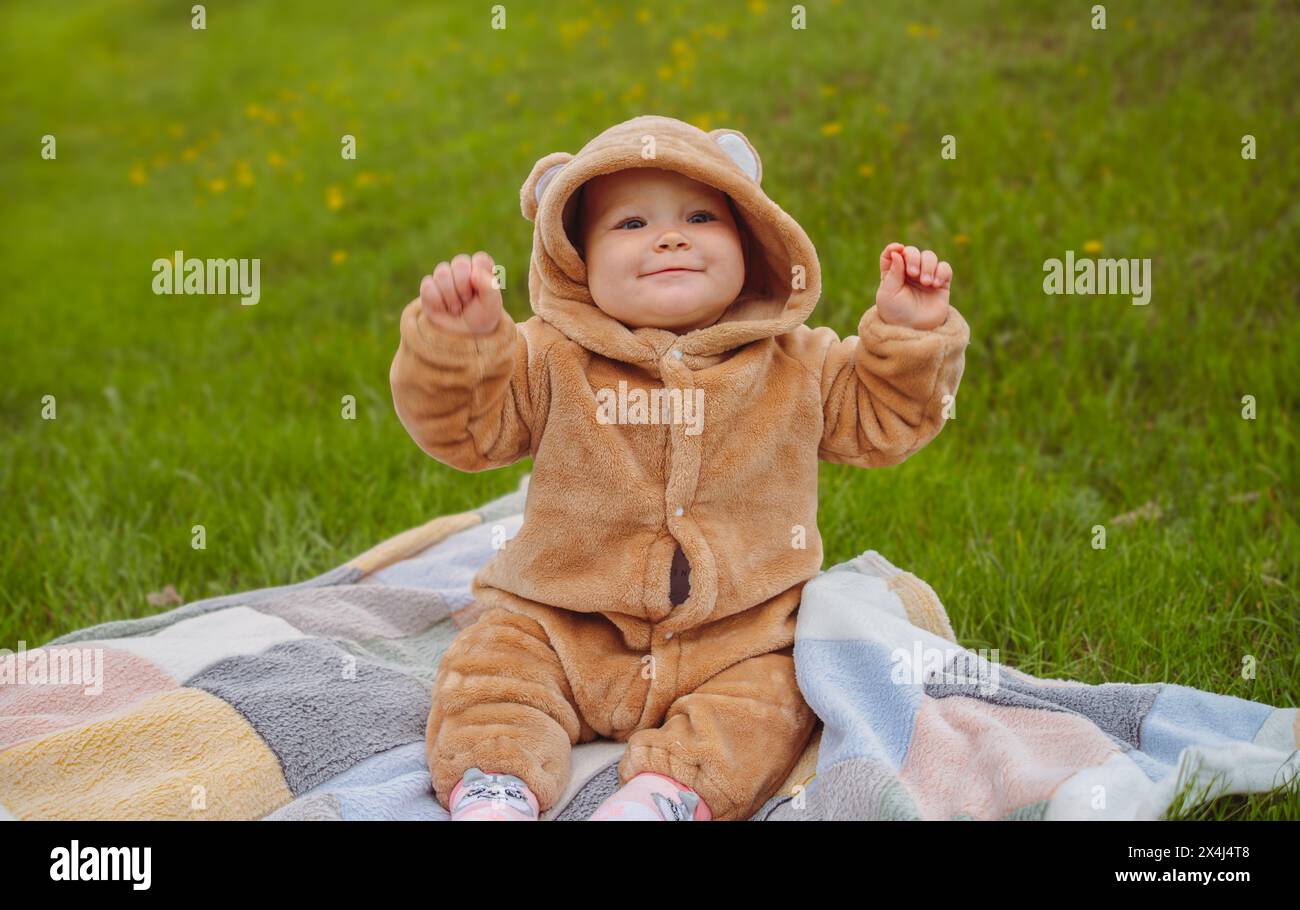 Baby im Bärenkostüm, das auf Decke sitzt. Ein Baby in einem Bärenkostüm, das auf einer Decke in einer gemütlichen Umgebung sitzt Stockfoto
