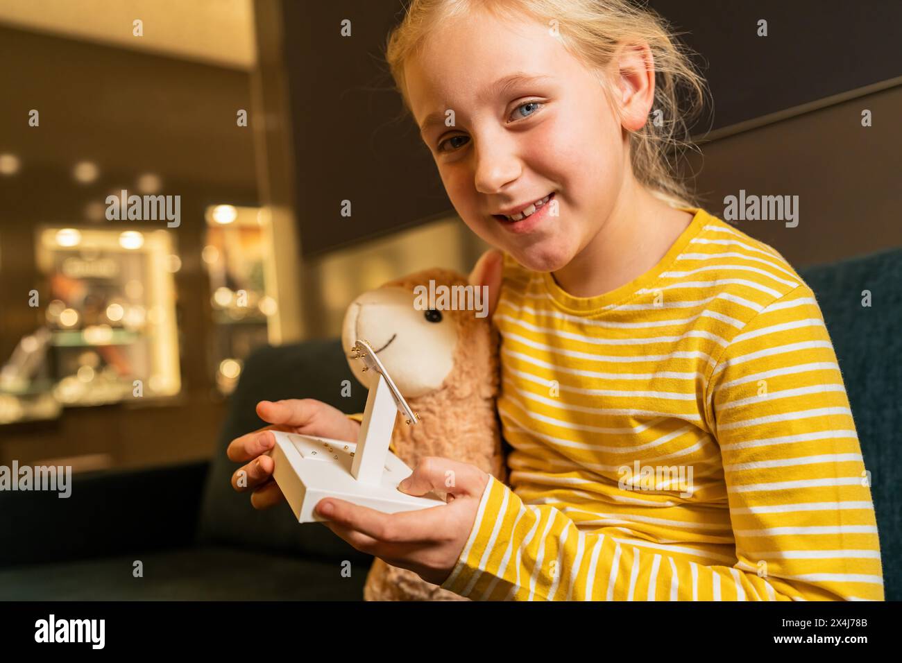 Glückliches Mädchen mit einem Plüschtier, das auf Ohrringe auf einem weißen Ständer im Juweliergeschäft schaut Stockfoto