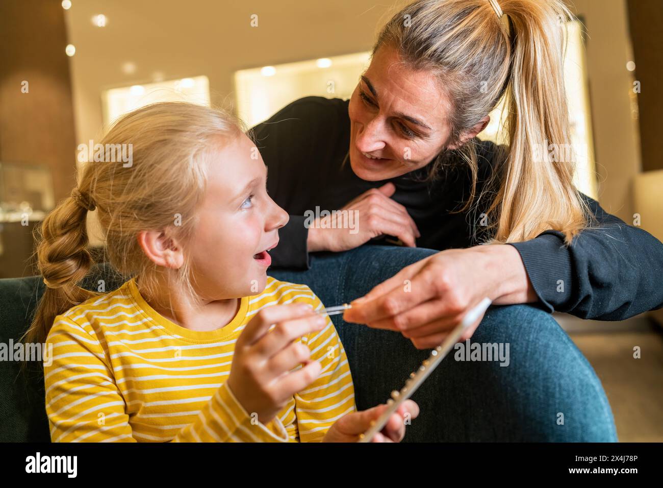Das aufgeregte Kind sieht Mutter an, während es neue Ohrringe zeigt, Mutter lehnt sich mit Interesse an einem Juweliergeschäft an Stockfoto