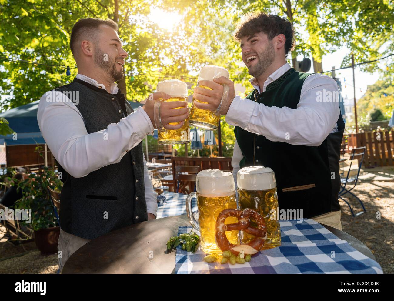 Zwei Männer in traditionellen bayerischen Outfits, die auf dem oktoberfest oder im Biergarten mit großen Bierkrügen anstoßen Stockfoto