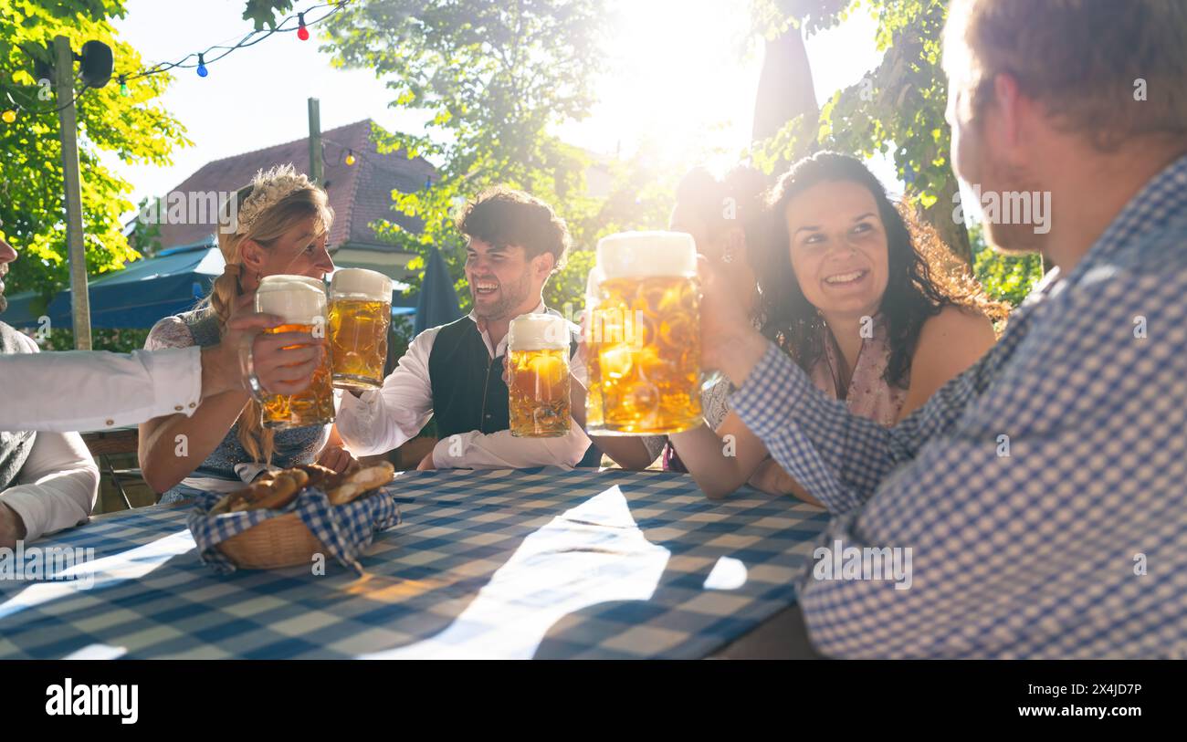 Lächelnde Menschen, die bei einem sonnigen Treffen im Freien im Biergarten oder auf dem oktoberfest Bierbecher anstoßen Stockfoto
