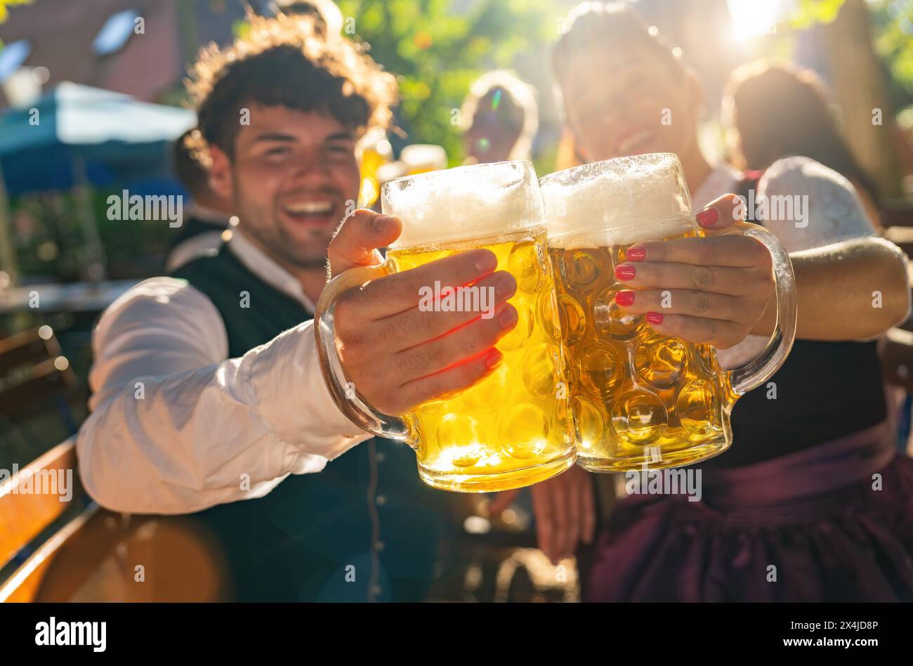 Zwei Personen in tracht, die Bierbecher klatschen und am sonnigen Tag auf dem oktoberfest oder Biergarten in deutschland lächeln Stockfoto