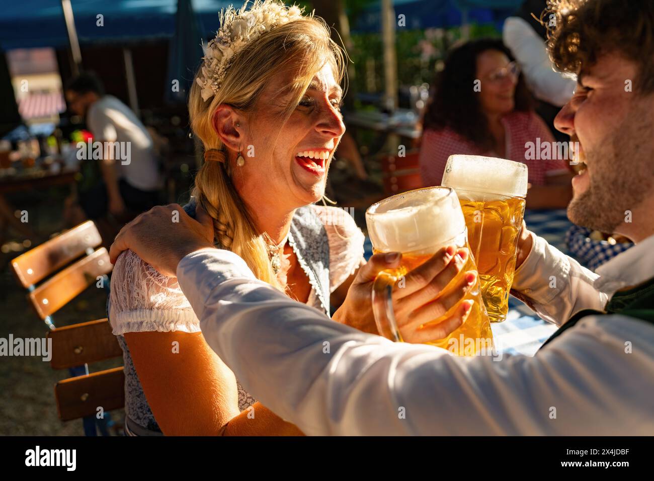 Ein paar lachende und toastende Bierbecher auf dem Oktoberfest, mit goldenem Hinsenlicht und verschwommenem Hintergrund in bayern Stockfoto