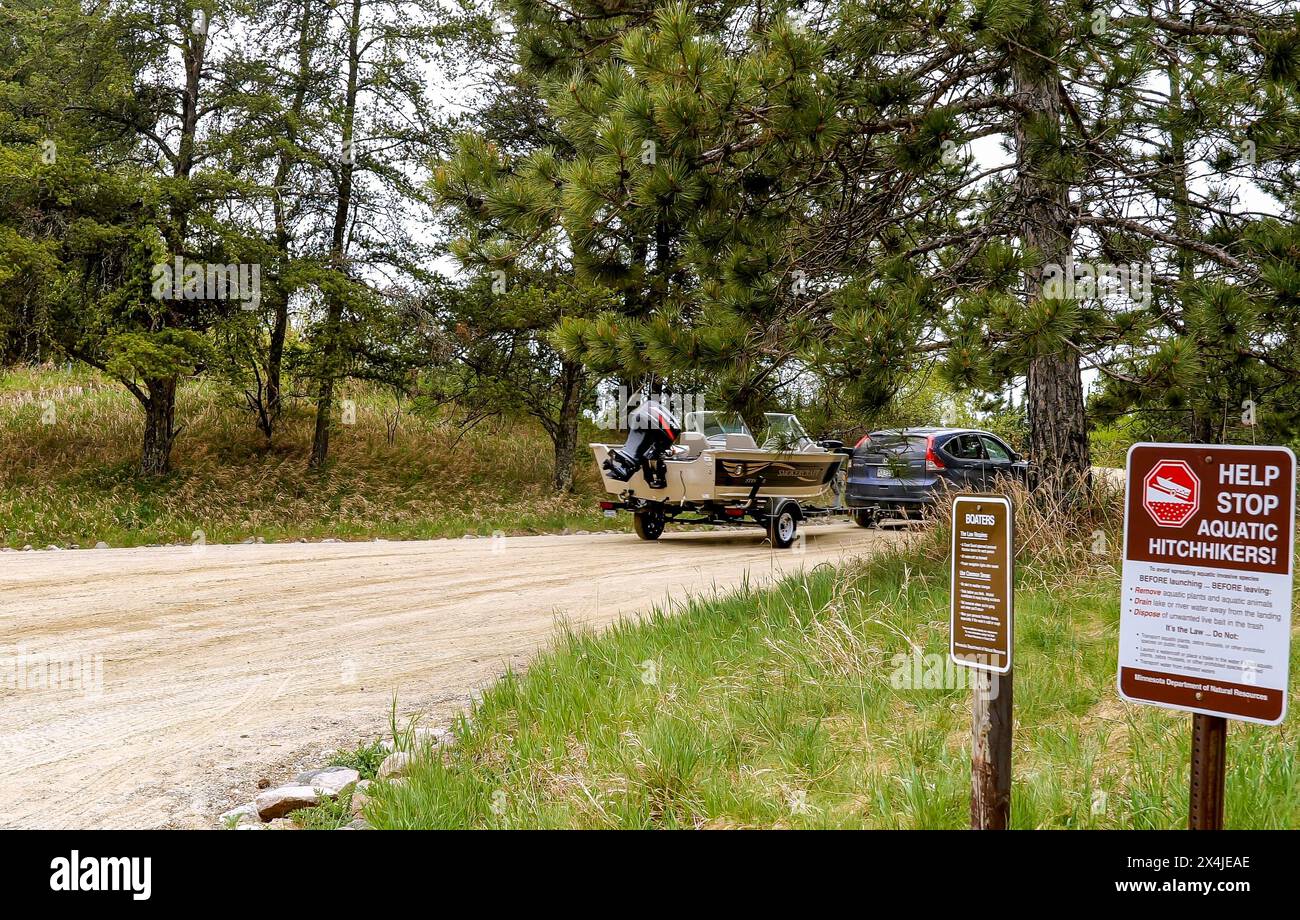 CLEARWATER CO, MN - 23. MAI 2020: Auto zieht Fischerboot und Anhänger auf einer Schotterstraße in der Nähe eines Minnesota Sees und vorbei an Schildern über invasives sp Stockfoto