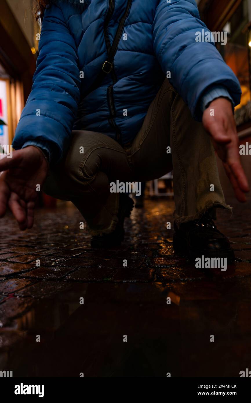 Weibliche Füße in blauen Sneakers spiegeln sich abends in einer Pfütze einer Stadtstraße Stockfoto