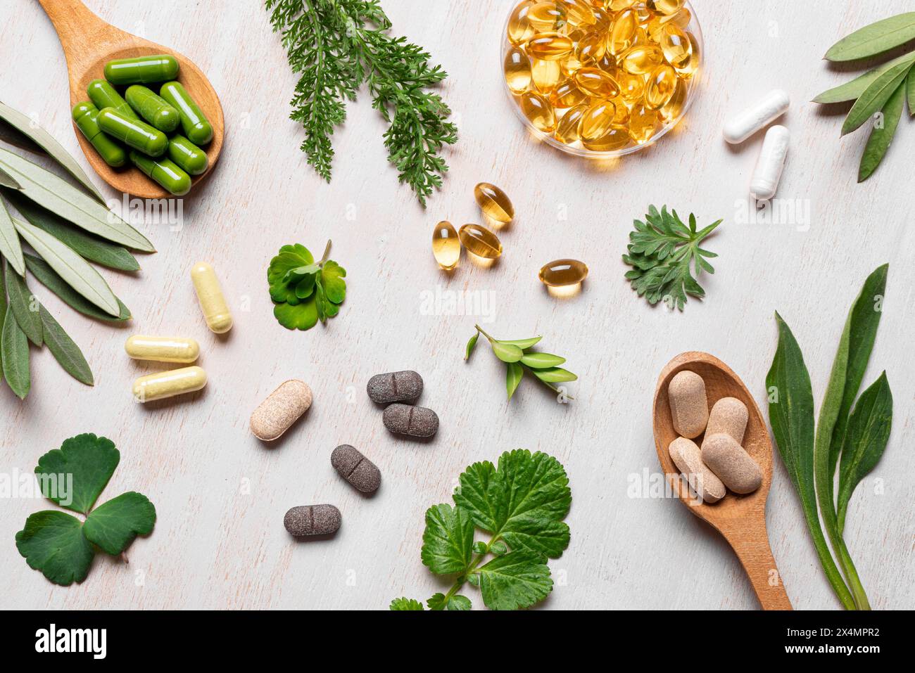 Natürliche Vitamine, pflanzliche Nahrungsergänzungsmittel und grüne Blätter liegen flach auf weißem hölzernem Hintergrund. Verschiedene Bio-Kapseln und -Pillen. Stockfoto