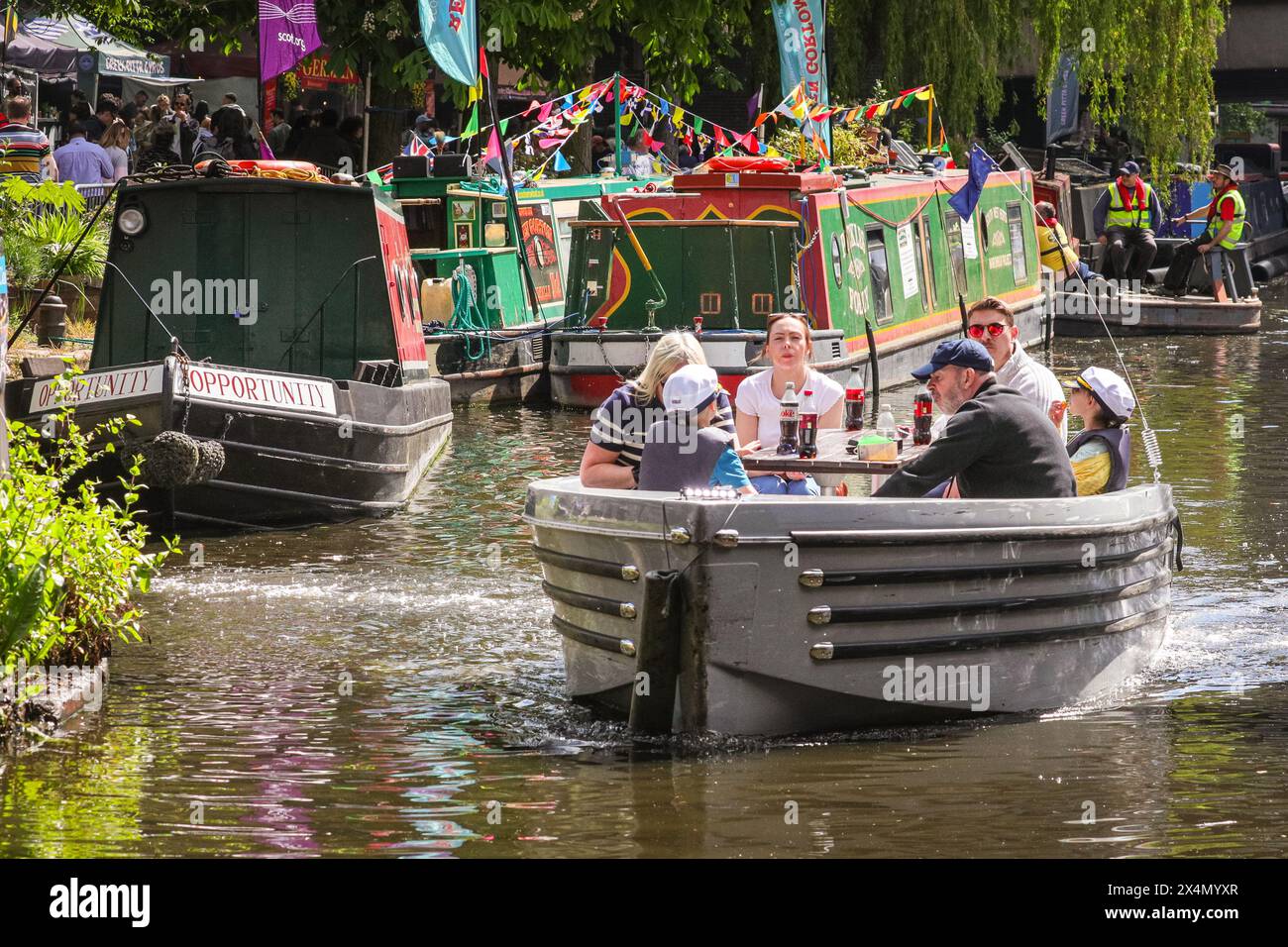 London, Großbritannien. Mai 2024. Ein Vergnügungsboot fährt an den aufgereihten Kanalbooten vorbei. Die jährlich stattfindende IWA Canalway Cavalcade kehrt zum Feiertagswochenende Anfang Mai nach Little Venice zurück und feiert die Britains Waterways und ihre Gemeinde. Es bietet rund 100 dekorierte Boote, einen Wasserstraßenzug, Aktivitäten und Unterhaltung. Quelle: Imageplotter/Alamy Live News Stockfoto