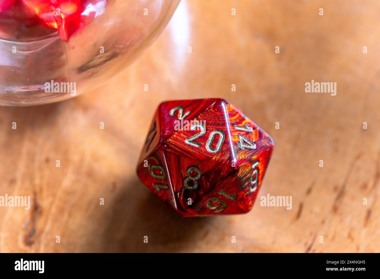 Nahaufnahme einer leuchtend roten D20-Matrize, die ihre detaillierten Markierungen auf einem warmen Holzhintergrund betont und perfekt für Spiele und Fantasy-Themen geeignet ist. Stockfoto