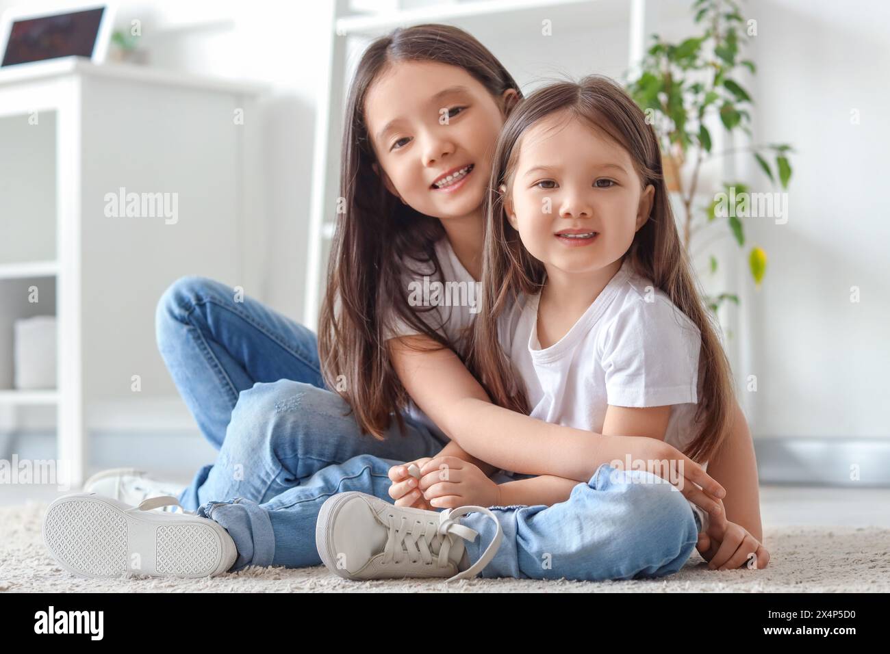 Süße kleine asiatische glückliche Schwestern, die sich zu Hause auf dem Boden umarmen Stockfoto