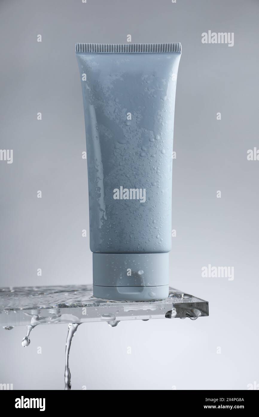Feuchtigkeitsspendende Creme in der Tube auf Glas mit Wassertropfen vor grauem Hintergrund Stockfoto
