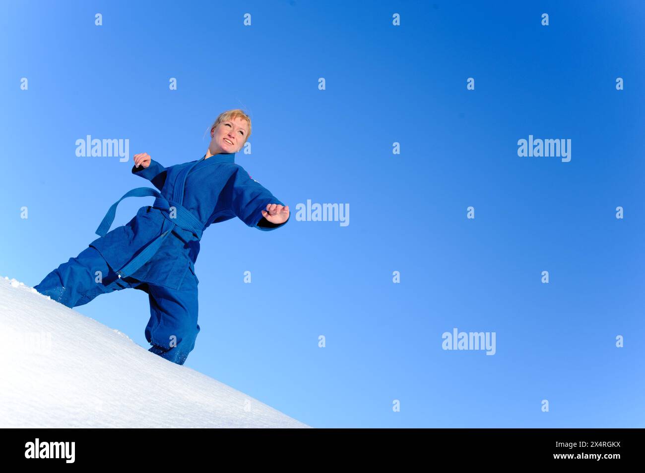 Junge Frau in blauem Kimono steht auf Schnee und bereit zum Kampf Stockfoto