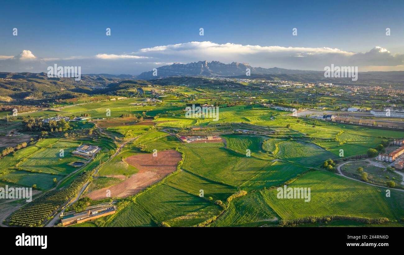 Blick aus der Vogelperspektive auf die grünen Felder von Pla de Bages bei Sonnenuntergang im Frühling. Im Hintergrund der Berg Montserrat (Bages, Barcelona, ​​Catalonia, Spanien) Stockfoto