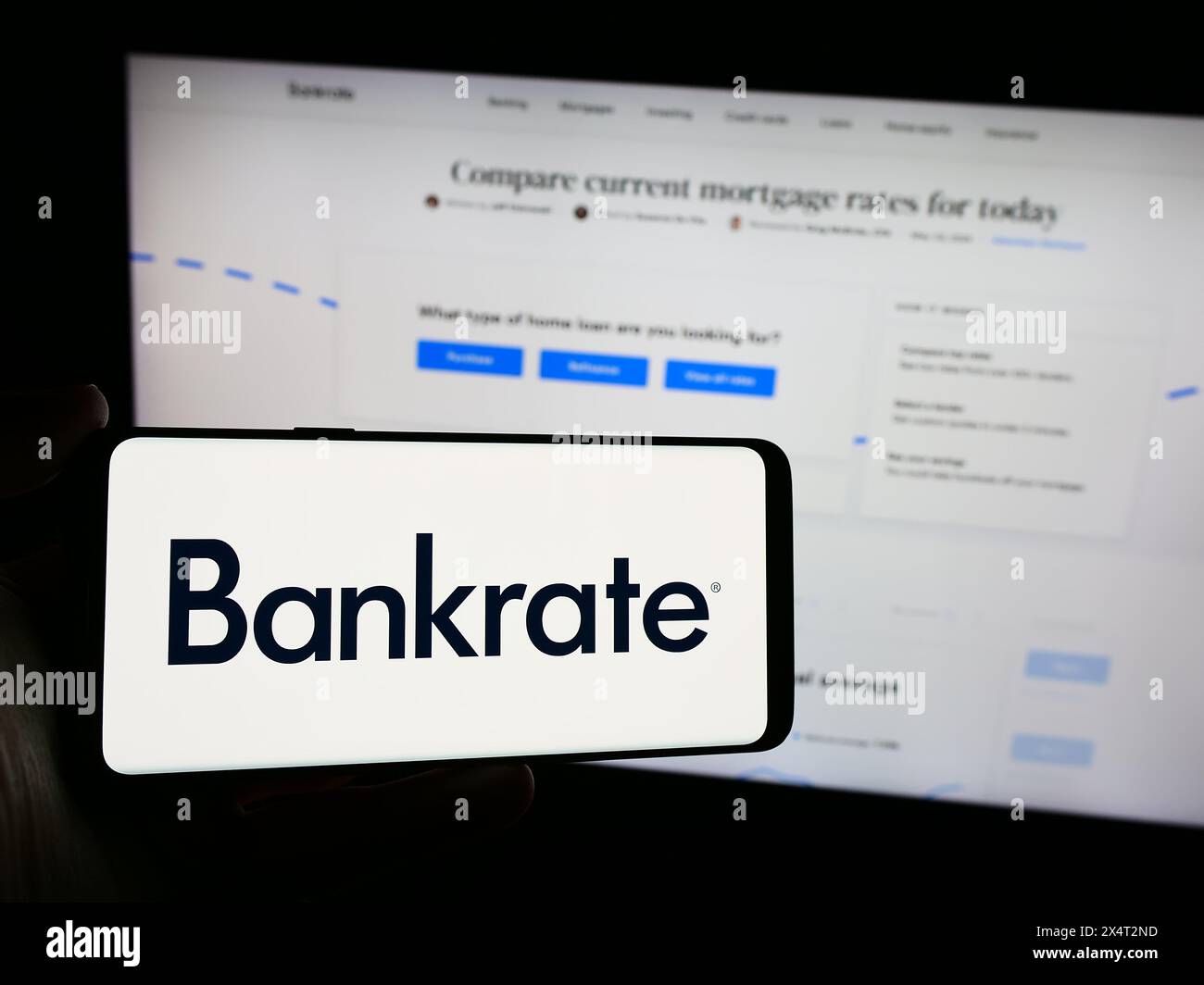 Person, die ein Mobiltelefon mit dem Logo des amerikanischen Finanzunternehmens Bankrate LLC vor der Webseite des Unternehmens hält. Schwerpunkt auf dem Display des Telefons. Stockfoto