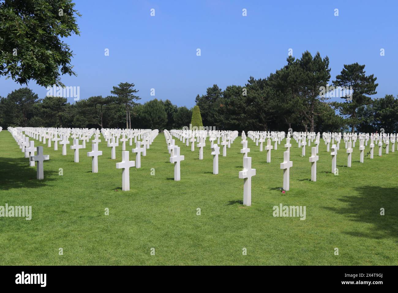 Linien von weißen Marmorkreuzen auf grünem Gras auf dem Kriegsfriedhof. Umliegende Wälder und blauer Himmel, aber keine sichtbaren Menschen. Stockfoto