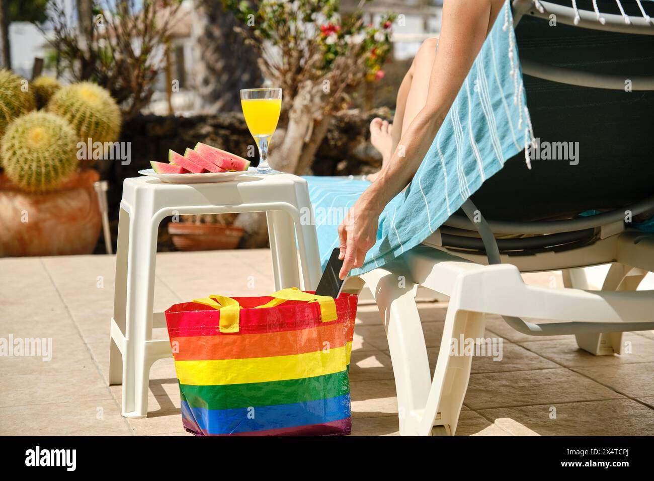 Unerkennbare Frau auf Liege mit Regenbogenbeutel Stockfoto