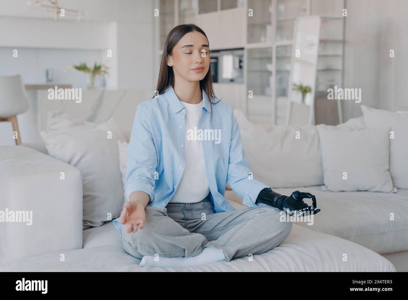 Eine ruhige Frau mit Roboterarm meditiert auf der Couch und verbindet Ruhe mit moderner Technik. Stockfoto