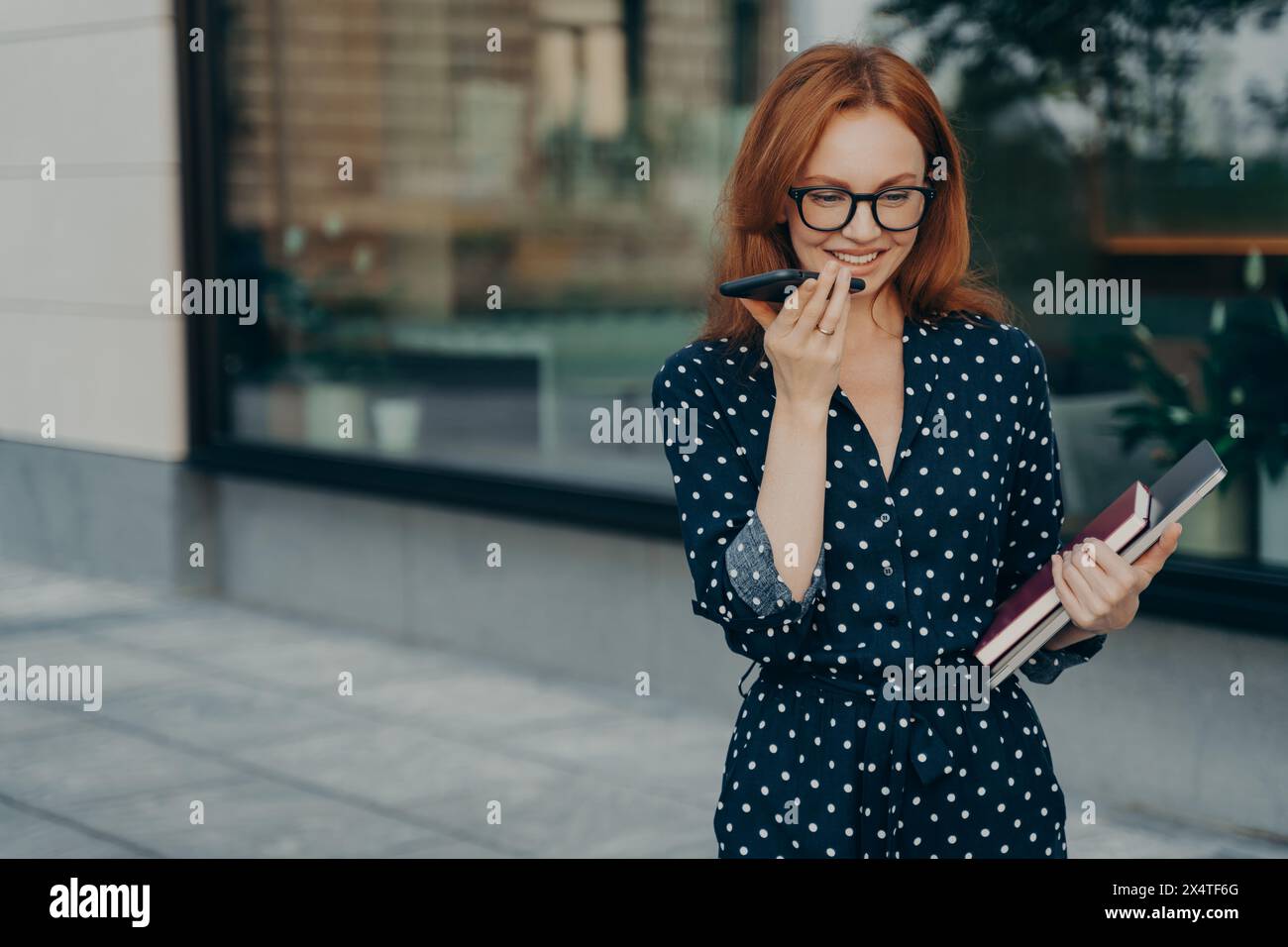 Lächelnde Profi-Frau mit Voice Recorder auf einem Smartphone mit Notebook in der Hand. Stockfoto