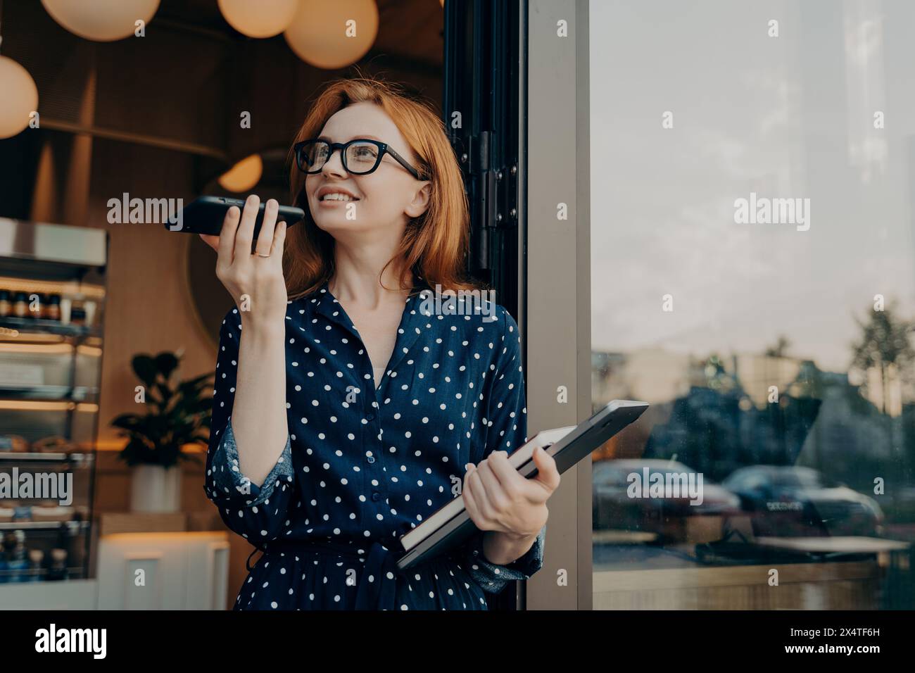 Neugierige Frau mit Freisprechfunktion vor dem Café, die sich mit moderner Technologie beschäftigt. Stockfoto