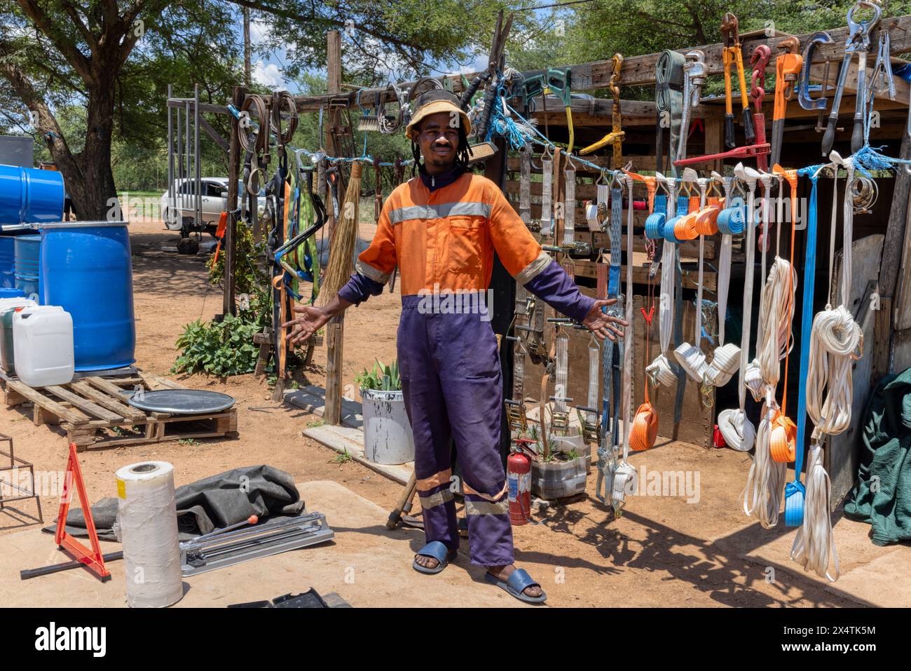 afrikanischer Straßenhändler, der neben der Straße Hardware verkauft, trägt orangefarbene Arbeitskleidung und Dreadlocks-Zöpfe Stockfoto