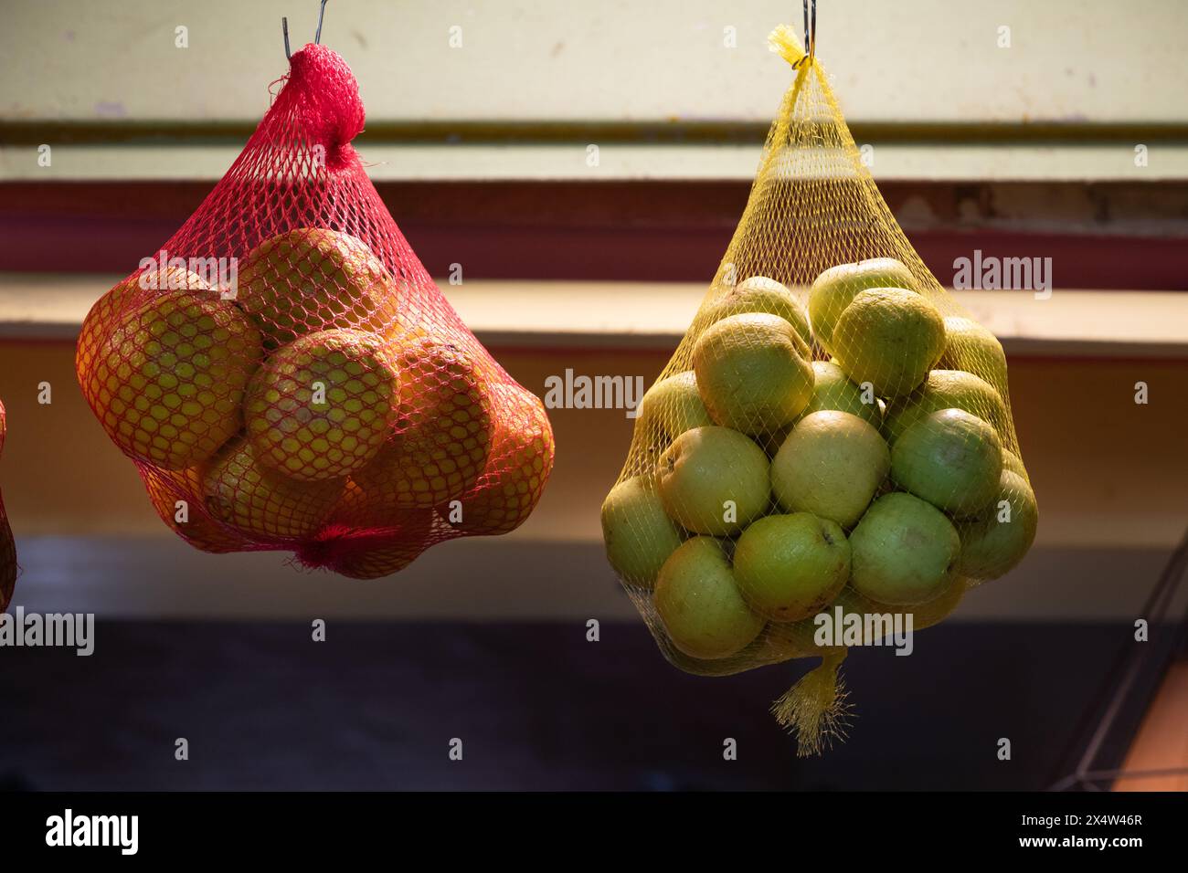 Hängende Netzsäcke, in denen frische Orangen und Äpfel an einem Saftstand aufbewahrt werden. Stockfoto