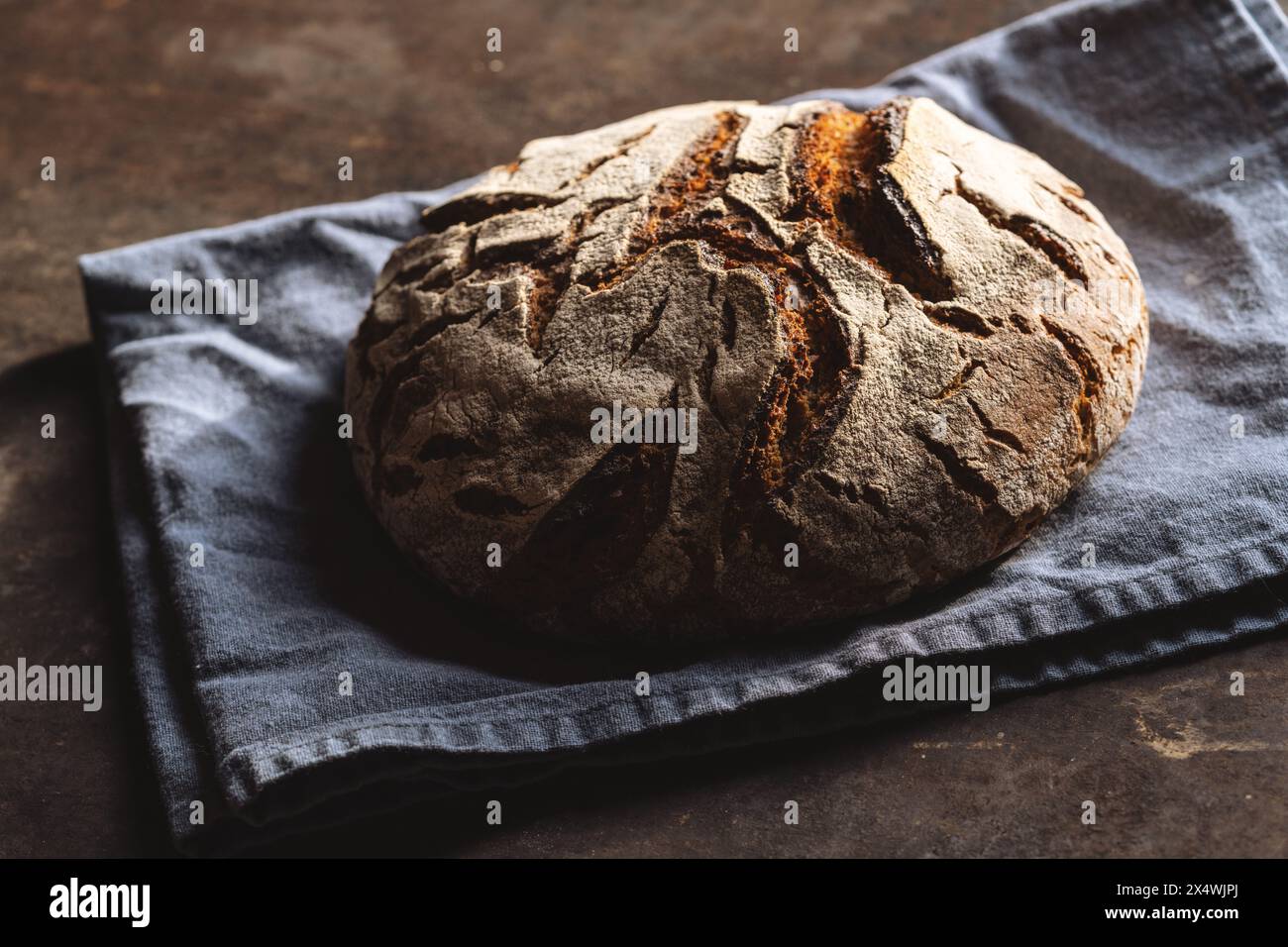 Nahaufnahme eines knusprigen Sauerteigbrotes auf einer blauen Leinenserviette, auf einer dunklen strukturierten Oberfläche Stockfoto