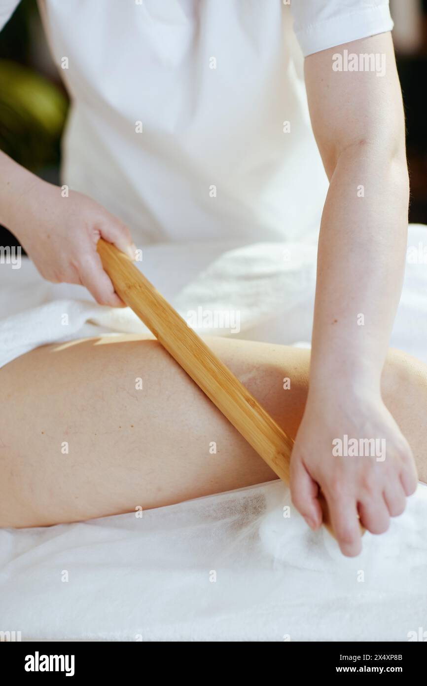 Gesundheitszeit. Nahaufnahme eines Massagetherapeuten in Massagekabine mit Holzmassagestab, der das Bein des Kunden massiert. Stockfoto