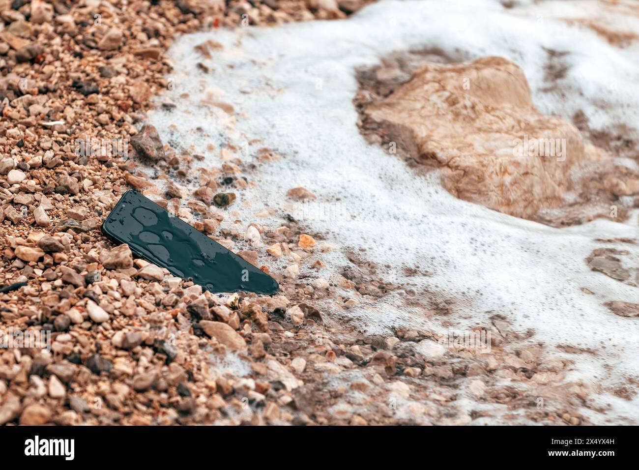 Verlorenes Handy am Meer, das von den Wellen am Strand gewaschen wurde, selektiver Fokus Stockfoto