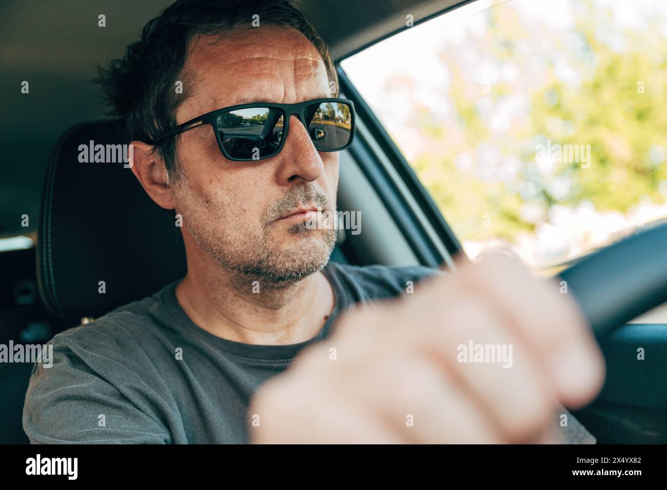 Coole Erwachsene männliche Fahrer mit schwarzer Sonnenbrille, die ein Auto entlang der Straße fährt, selektiver Fokus Stockfoto