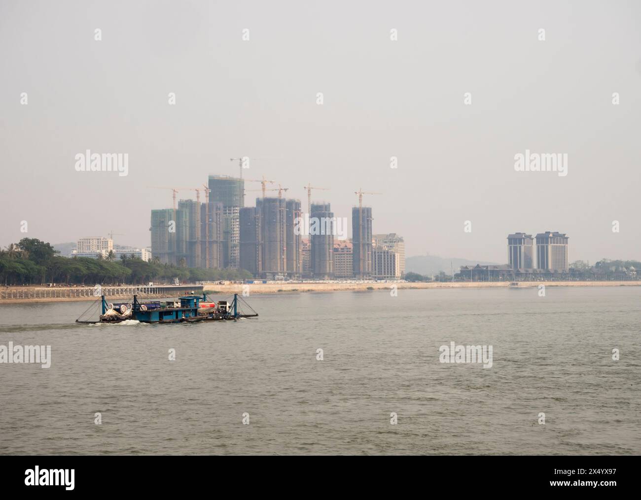 Van Pak Len, Laos - 28. März 2024: Ein Frachtschiff fährt an Wohnhäusern vorbei, die unter Bau stehen, am Ufer des Mekong. Stockfoto